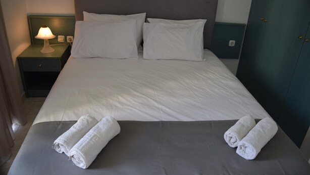 Een net opgemaakt bed met witte lakens en twee opgerolde handdoeken erop.