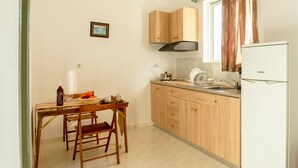 Een compacte keuken met houten kastjes, een witte koelkast, een eettafel met stoelen en een hangende lamp.
