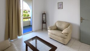 Een woonkamer met een salontafel met glazen blad, een beige bank en een deur naar een balkon.