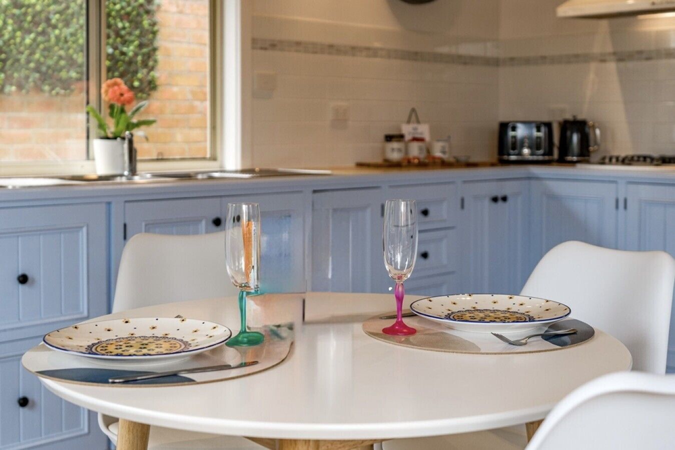 A kitchen with blue cabinets, a white table, two plates with a floral pattern, and two glasses.