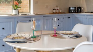 Une cuisine avec des meubles de rangement bleus, une table blanche, deux assiettes ornées de motifs floraux et deux verres.