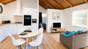 Une cuisine moderne avec des meubles blancs, une table à manger avec des chaises blanches, un canapé gris et un téléviseur.