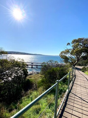 A paved walkway with a metal railing, overlooking a body of water and a bridge. - Back `O` Burke Victor Harbor (Victor Harbor)