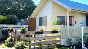 Une maison de plain-pied avec un porche à l’avant, une cour clôturée et un petit jardin agrémenté de fleurs et d’arbustes.