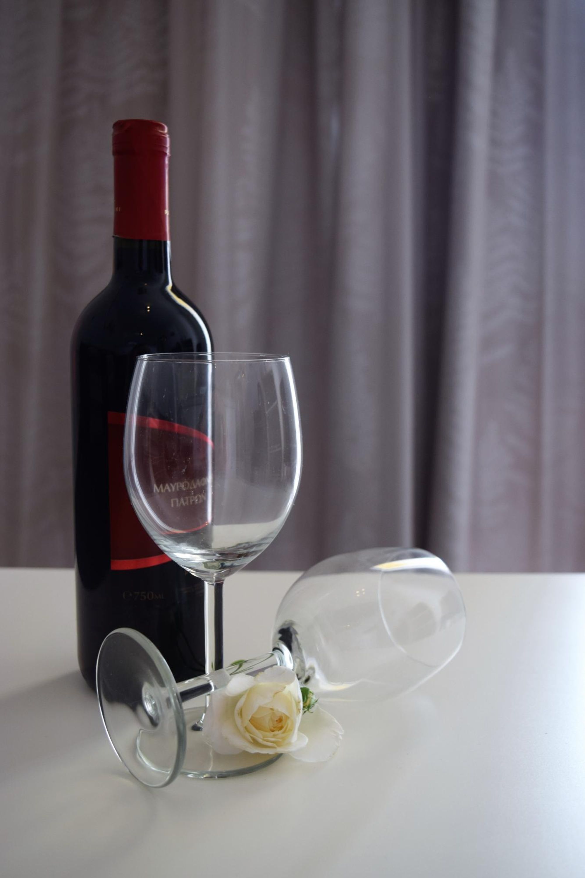 A wine bottle and a wine glass with a rose on a white table.
