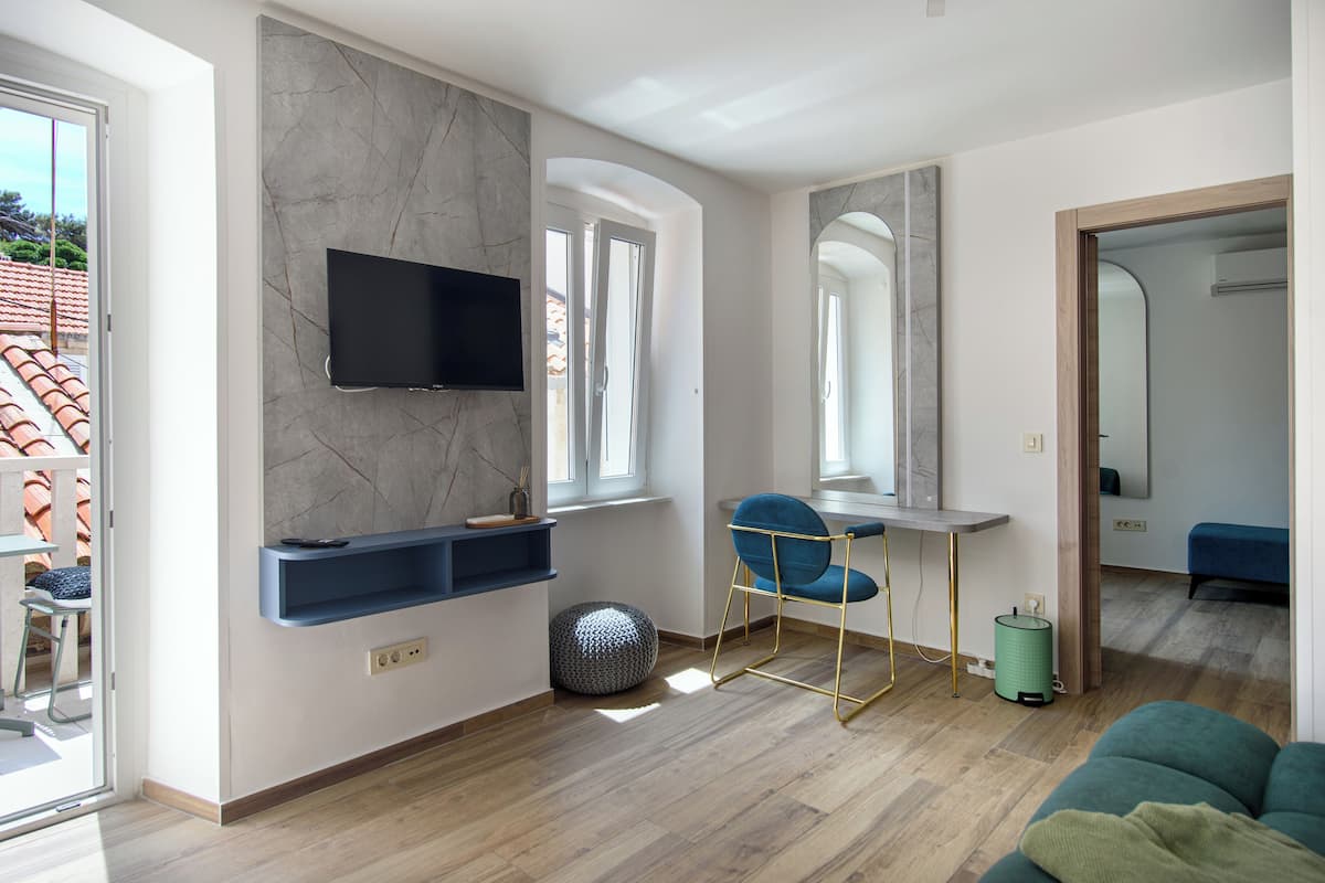 Un salón moderno con un televisor montado en una pared de mármol, un sillón azul, una mesita y un cubo de basura verde.