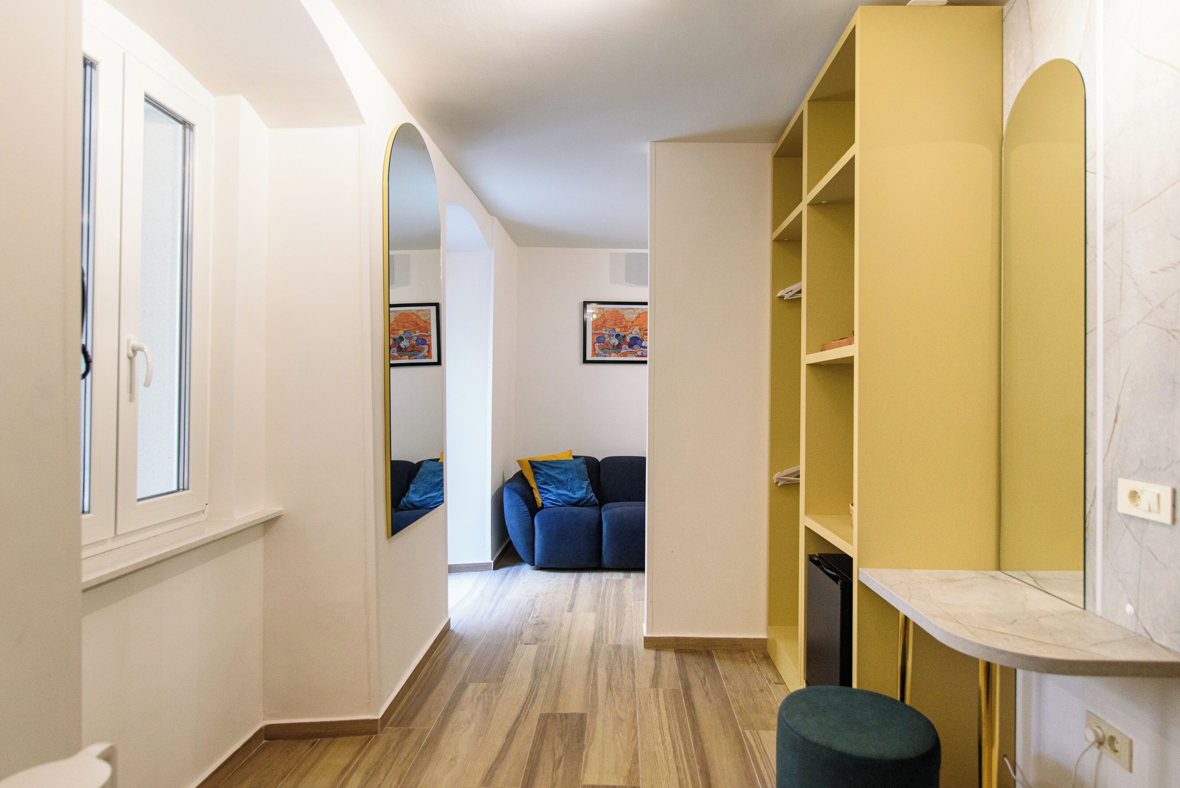 Un couloir avec un canapé, une petite table et une étagère jaune.