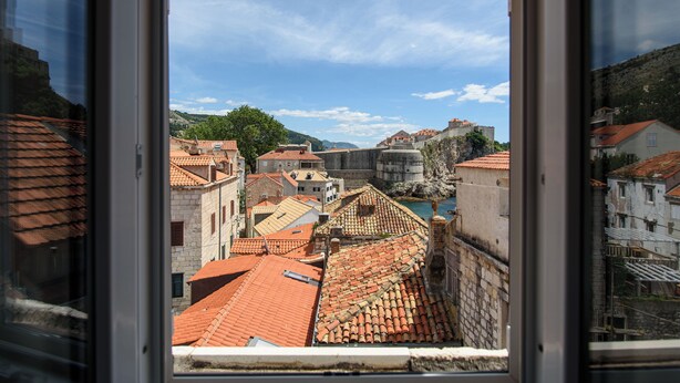 Una vista di una città storica con edifici a tetto in terracotta e un castello imponente sullo sfondo.
