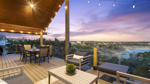 An outdoor deck with a dining area, seating, and a view of a landscape with water and buildings. - The Sanctuary at Canyon Lake | 3 Bed, 3 Bath (Canyon Lake)