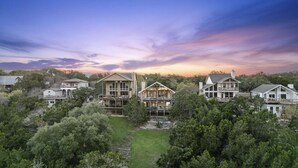 A residential area with multiple houses, featuring a central house with a large deck and a second-story balcony, surrounded by dense greenery. - The Sanctuary at Canyon Lake | 3 Bed, 3 Bath (Canyon Lake)