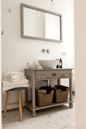 A bathroom with a white sink, a mirror, and a wooden vanity. There are towels stacked on a stool and baskets under the vanity. - Ca Bela Lambrate (Milan)