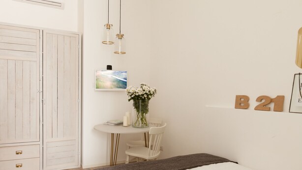 Un dormitorio con cama, mesita de noche con un florero, una pequeña mesa con una silla, televisor y armario.