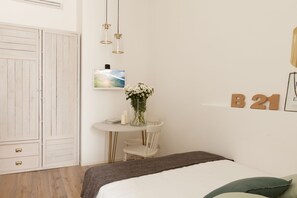 A bedroom with a bed, a bedside table with a vase of flowers, a small table with a chair, a TV, and a wardrobe. - Ca Bela Lambrate (Milan)