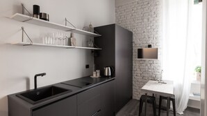 Una cocina moderna con armarios oscuros, estantes blancos y una pared de ladrillo decorativa.