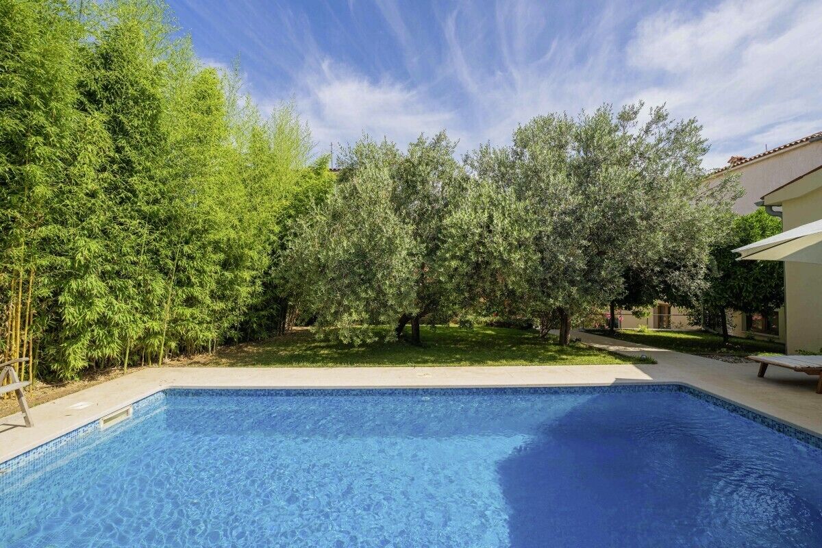 Une piscine entourée d’une végétation luxuriante et un bâtiment doté d’un toit en tuiles.