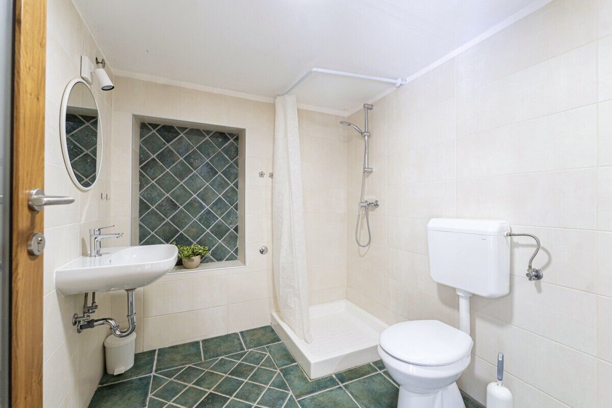 Ein Badezimmer mit Waschbecken, Toilette, Dusche und einem kleinen Fenster mit Pflanze.