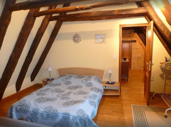 A bedroom with a sloped ceiling, a bed with a patterned bedspread, two bedside lamps, a clock, and a small painting on the wall. - Périgourdine House (Le Bugue)