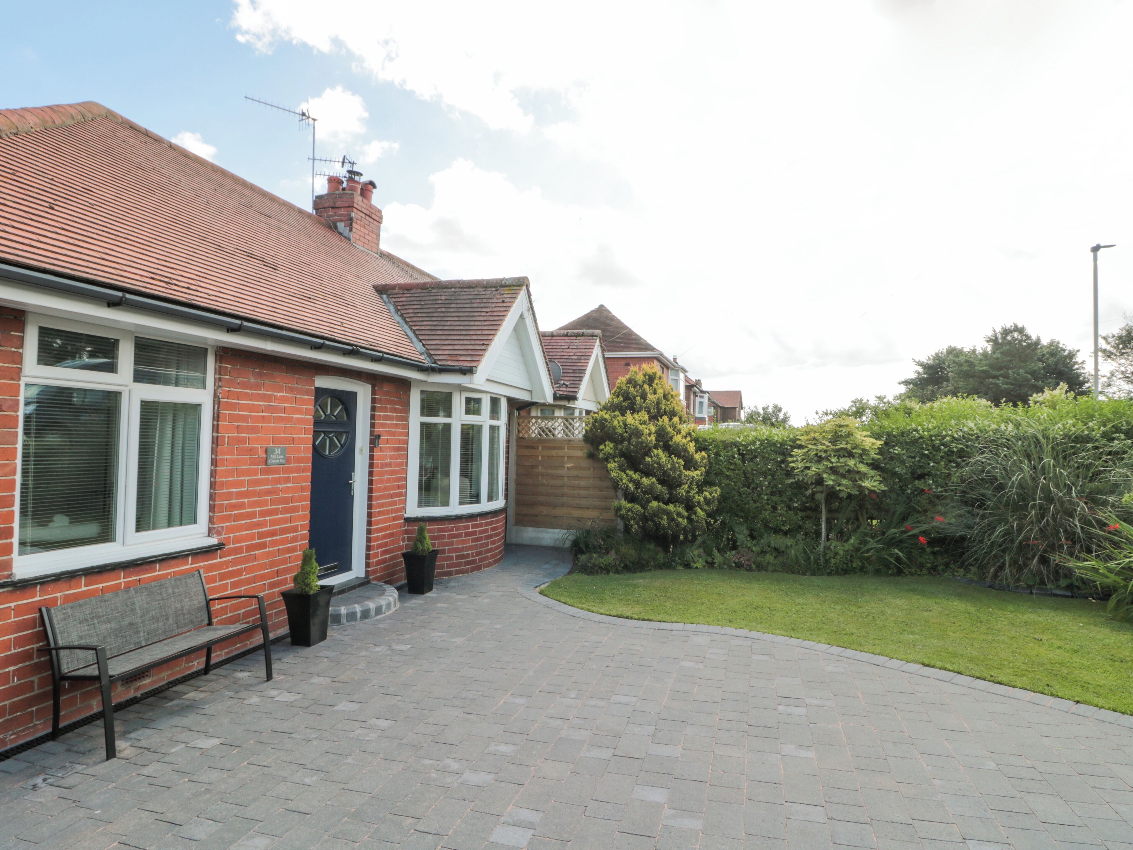 A residential house with a paved driveway, a bench, and a garden.