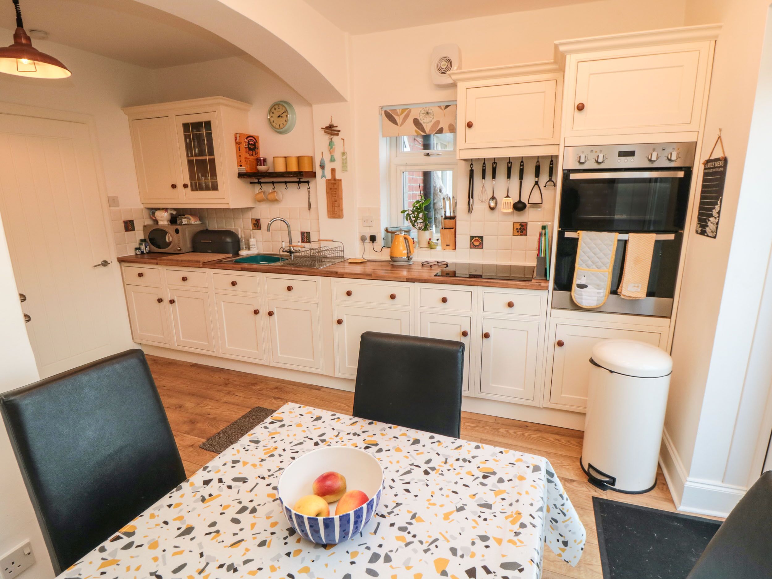 A kitchen with white cabinets, a sink, a stove, and a dining table with a bowl of fruit.