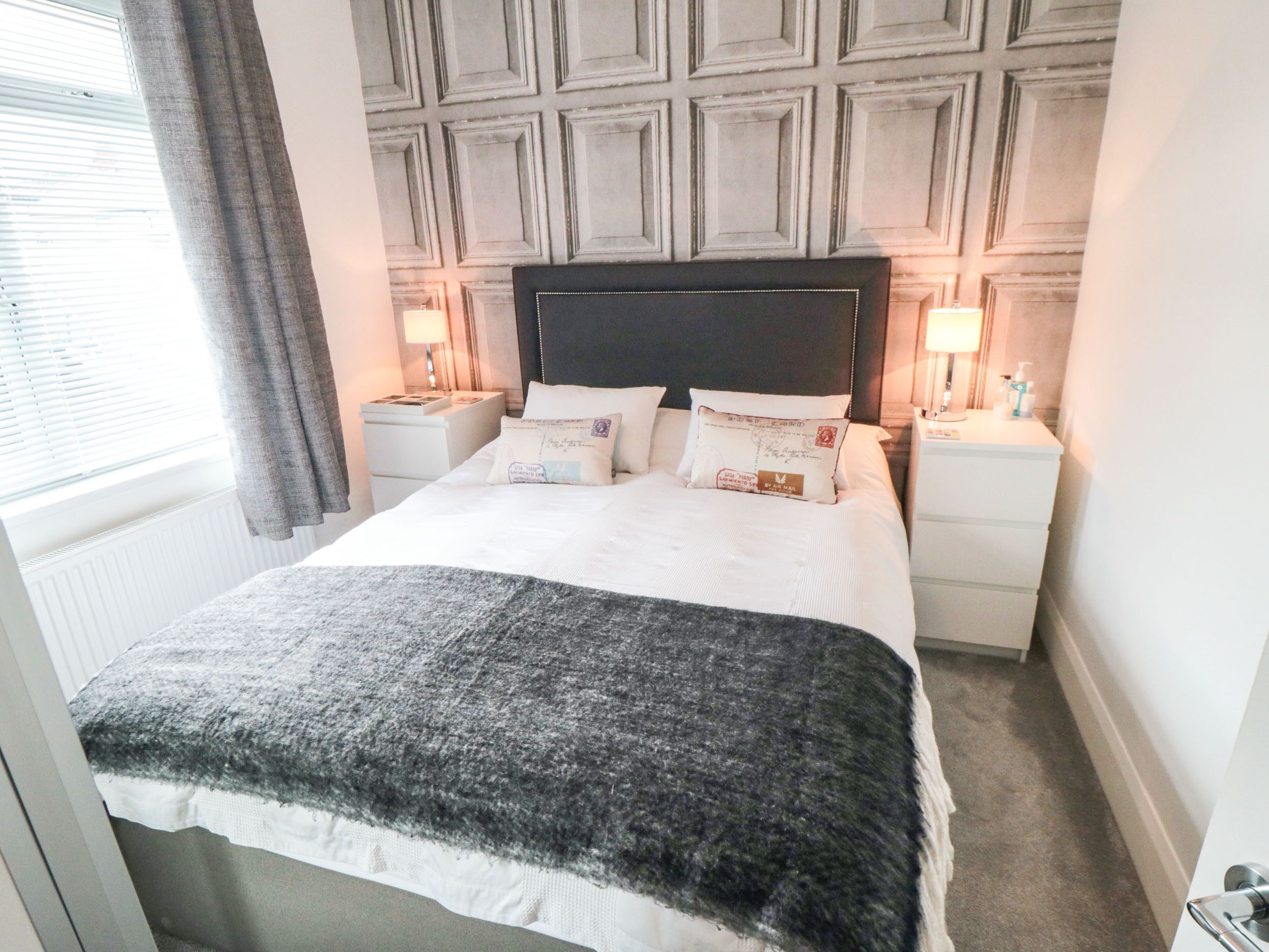 A neatly made bed with a black and white blanket, two bedside tables with lamps, and a wall with a geometric pattern.
