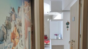 A hallway leading to a bedroom with a cityscape mural, a bed, and a bedside table with a lamp. - Depie Luxury Apartment in Pastida Rhodes (Rhodes)