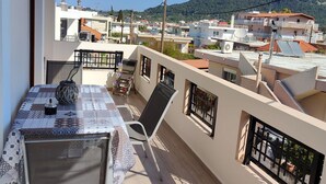 A balcony with a table and chairs, overlooking a residential area with houses and a mountain in the background. - Depie Luxury Apartment in Pastida Rhodes (Rhodes)