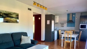 A modern living room with a sofa, a dining table, and chairs. There is a kitchen area with cabinets and a microwave.