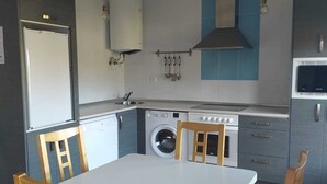 A compact kitchen with a washing machine, a stove, and a dining table with chairs.