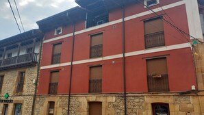 A multi-story building with a red facade and stone base, featuring multiple windows and balconies.