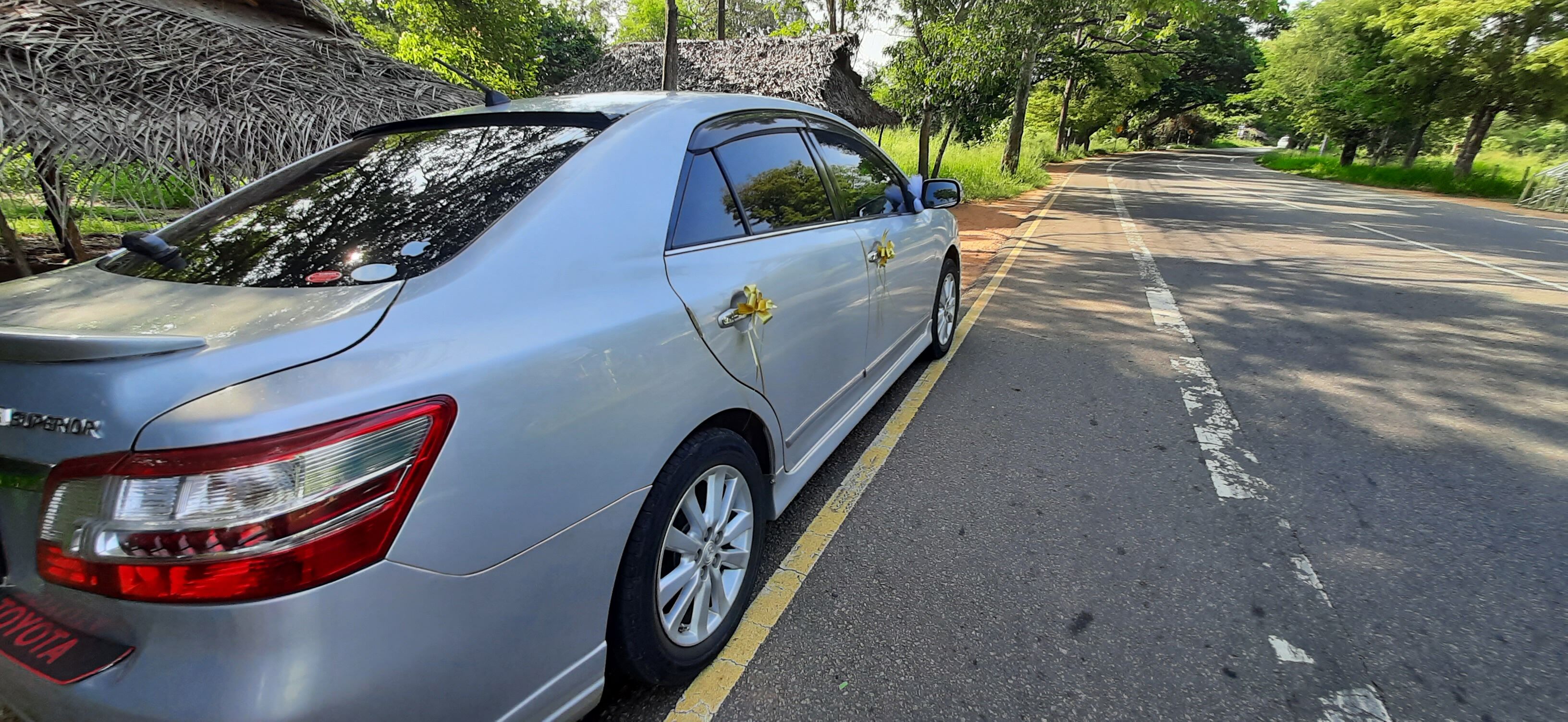 A silver Toyota sedan parked on a road with a yellow line on the side.