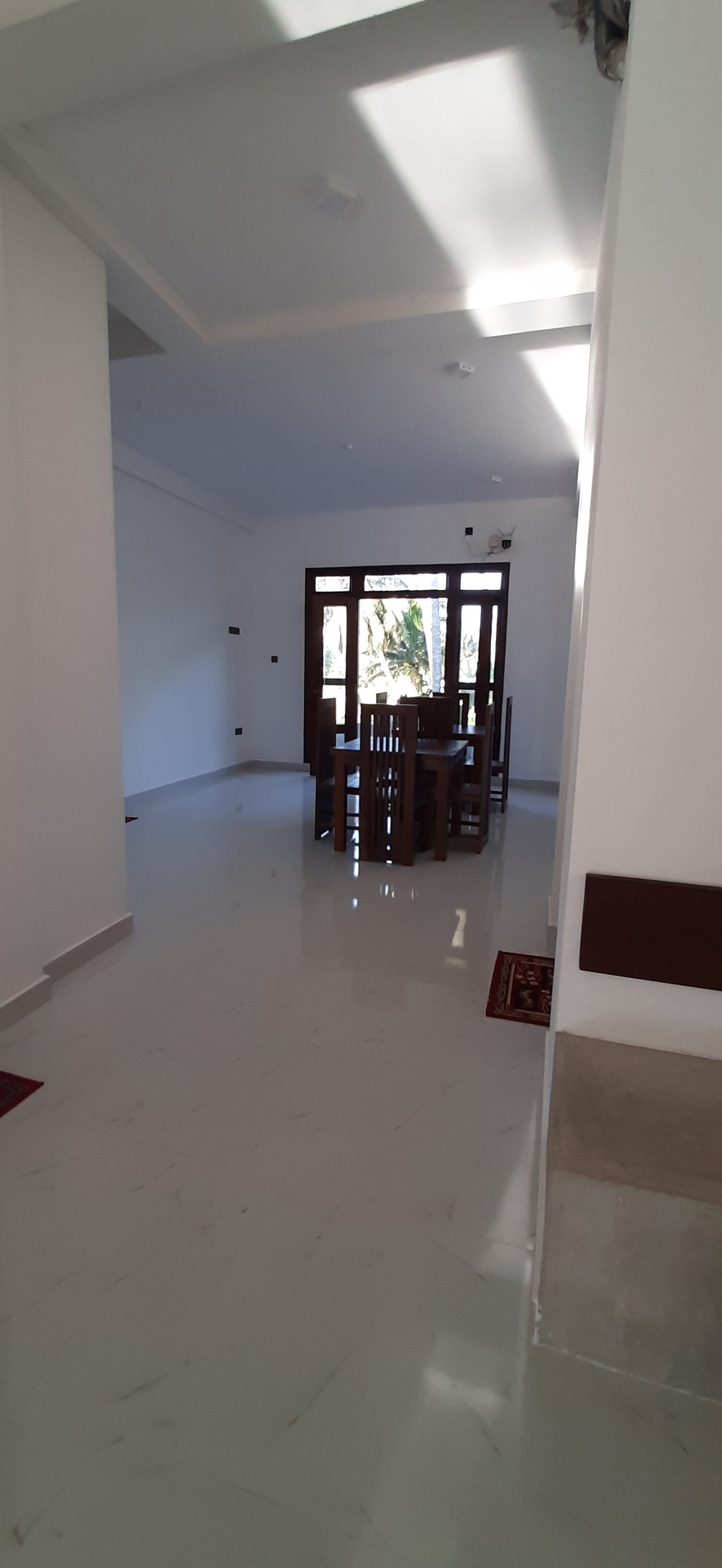 A spacious, well-lit room with a dining area featuring wooden furniture and a large window providing natural light.