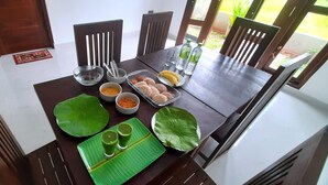 Une table à manger sur laquelle on trouve une variété de plats, notamment une assiette de bananes, des bols remplis de nourriture et un set de table vert en forme de feuille.