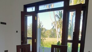 Un espace repas avec une table et des chaises en bois, de grandes fenêtres et une vue sur des palmiers.