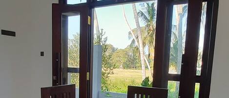 A dining area with a wooden table and chairs, large windows, and a view of palm trees.