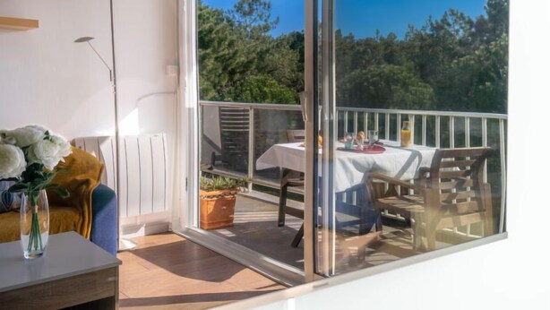 A balcony with a table set for dining, a potted plant, and a view of trees. - L'Ermitage by Interhome (Saint Brevin les Pins)