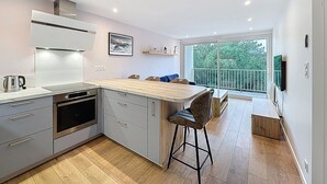 A modern kitchen with grey cabinets, a stainless steel range hood, and a wooden island with bar stools. - L'Ermitage by Interhome (Saint Brevin les Pins)