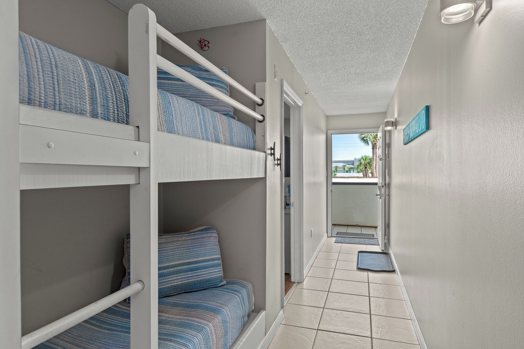 A hotel room with bunk beds, a door leading to a balcony, and a view of palm trees.