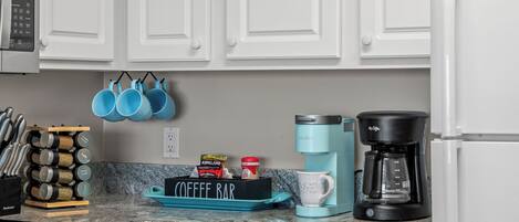 A kitchen with white cabinets, a coffee maker, a coffee pot, and a coffee bar sign.