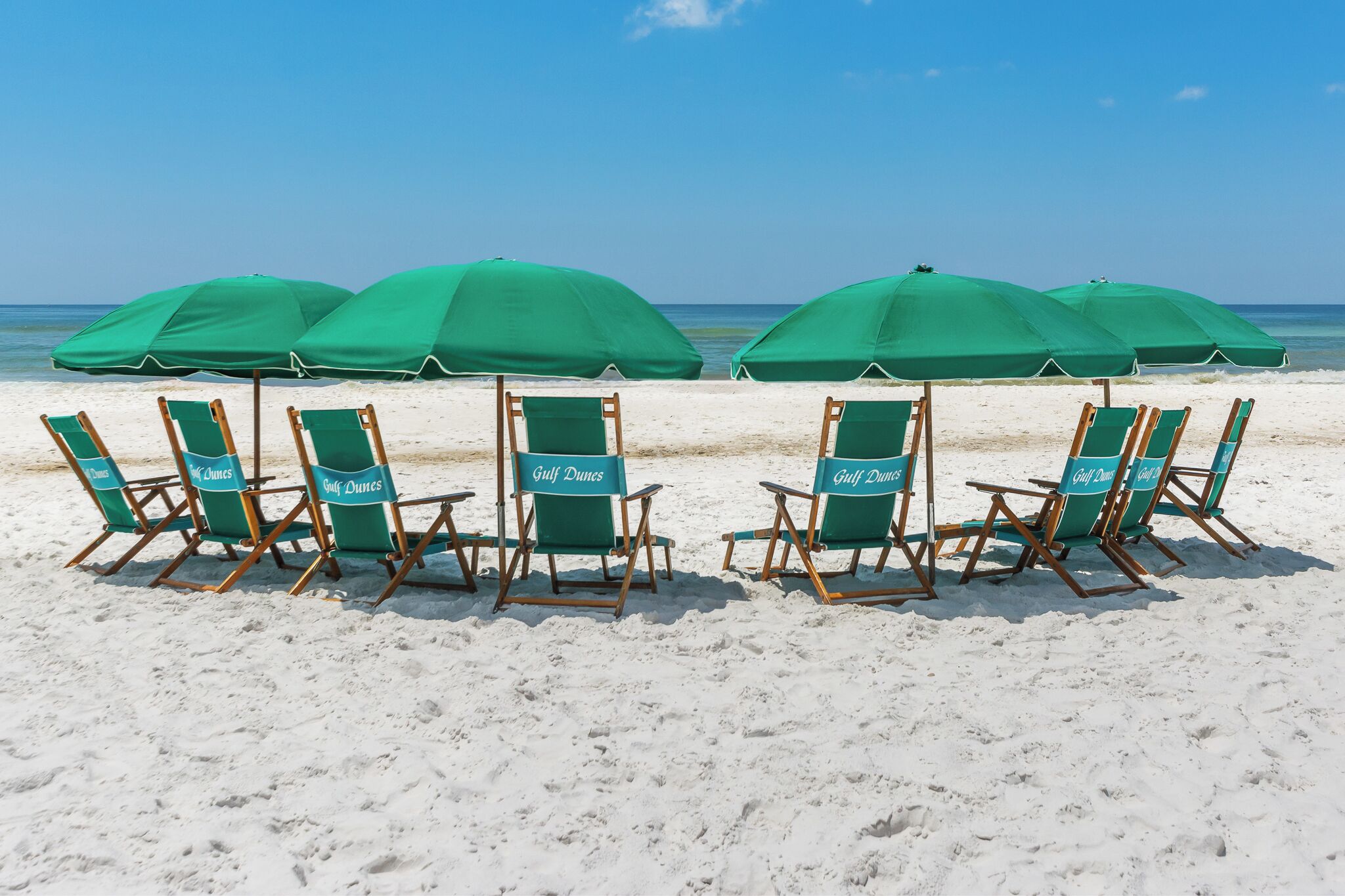 Una playa con hileras de sillas y sombrillas verdes, identificadas con el rótulo "Gulf Dunes".