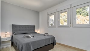 Une chambre à coucher avec un lit, une table de chevet et deux fenêtres donnant sur des arbres.