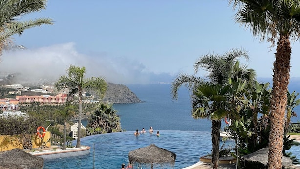 Une piscine avec vue sur la mer, entourée de palmiers et avec un bâtiment en arrière-plan.