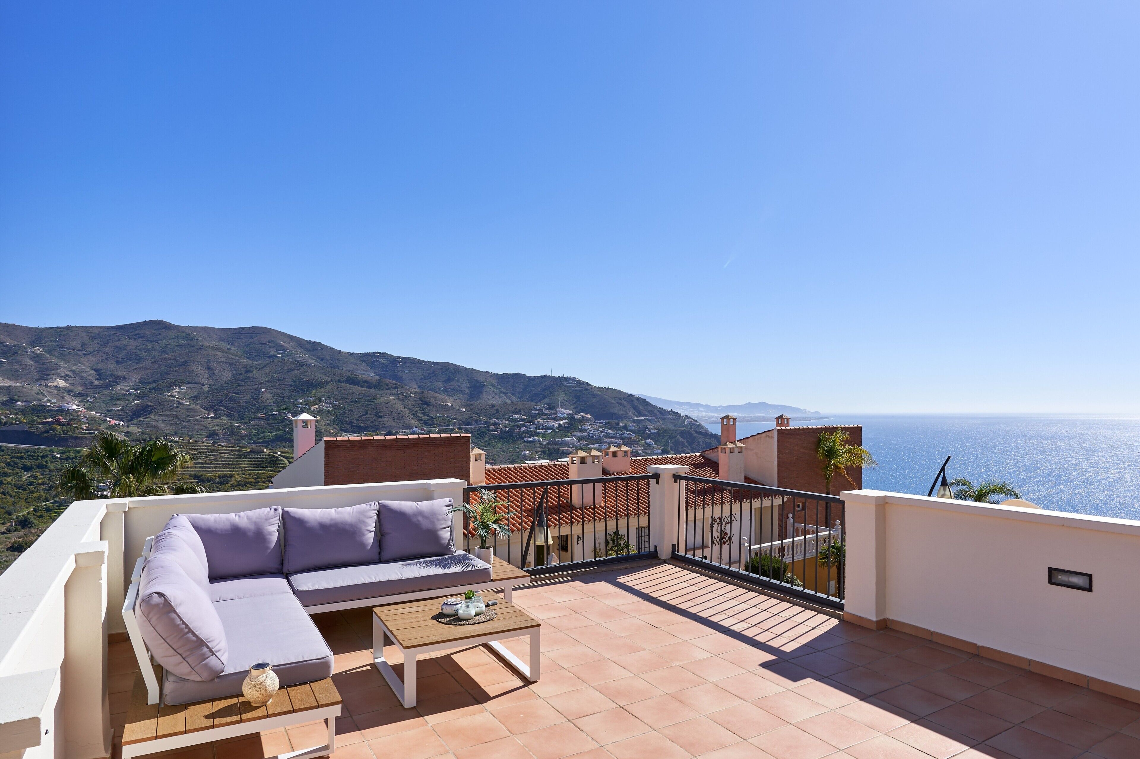 Un balcone con un divano, un tavolo e vista sul mare e sulle montagne.