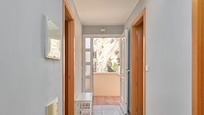 Un couloir avec un banc blanc, des portes en bois et une vue sur un balcon agrémenté de plantes.