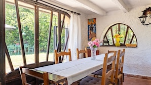 Un comedor con una mesa dispuesta para cuatro personas, sillas de madera, un jarrón con flores y un mural en la pared.