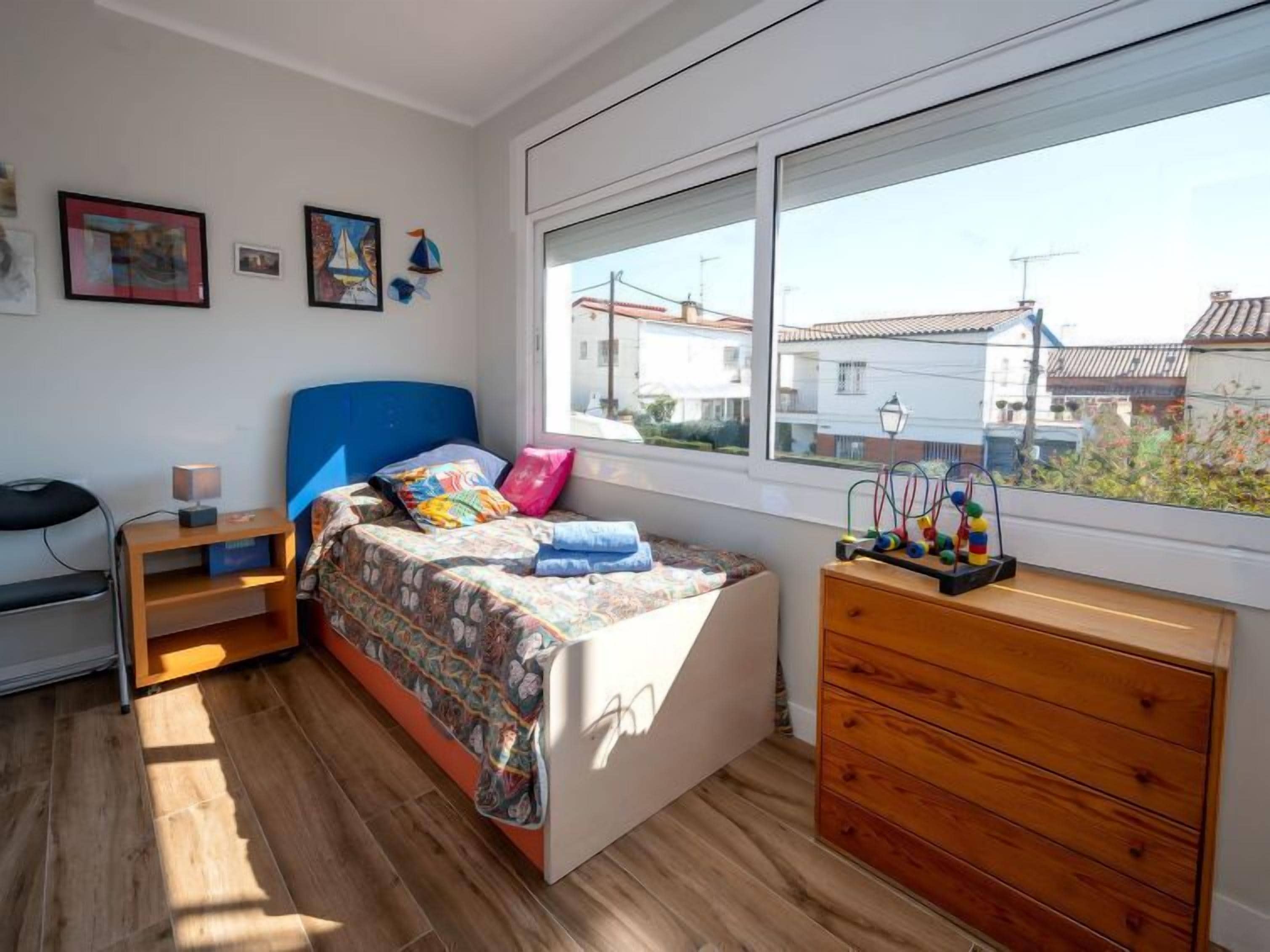 A bedroom with a bed, a dresser, a nightstand, and a window with a view of buildings.