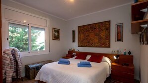 A bedroom with a large bed, a nightstand, a desk with a lamp, a red rug, and a window with a view of trees. - Millenium by Interhome (Premià de Dalt)