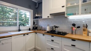 A modern kitchen with white cabinets, a wooden countertop, a gas stove, and a window with a view of trees. - Millenium by Interhome (Premià de Dalt)