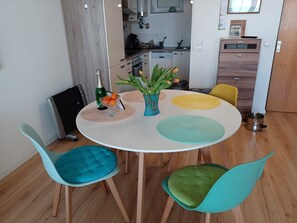 A dining area with a round table, four chairs, a vase with flowers, and a kitchen in the background.