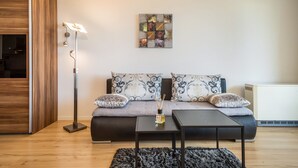 Een moderne woonkamer met een bank, twee bijzettafels, een vloerlamp en een kunstwerk aan de muur.
