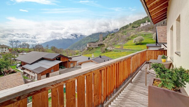 A balcony with a wooden railing overlooking a mountainous landscape with a castle-like structure in the distance.